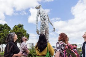 A large scale figure installation. Several people are looking up at it.