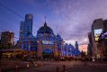 Flinders Street Railway Station in Melbourne - an Edwardian railway station with a dome as part of the city skyline at dusk. Across the front is a blue rectangular sign promoting the RISING arts festival.