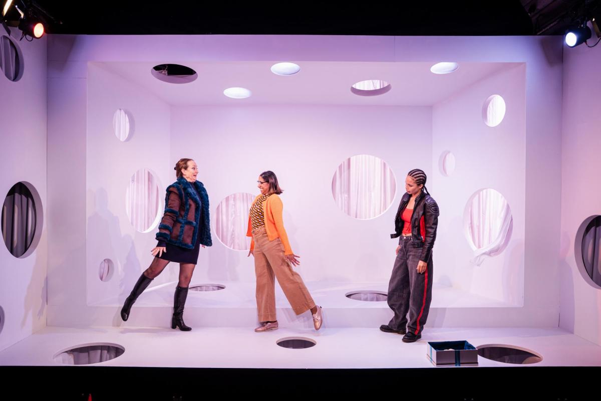 Three women in a white space with holes in the roof, floor and sides.