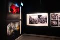 A exhibition display showing landscape photos an an angle on the left hand side and black photos of an army of soldiers on the back of the truck in the centre frame.