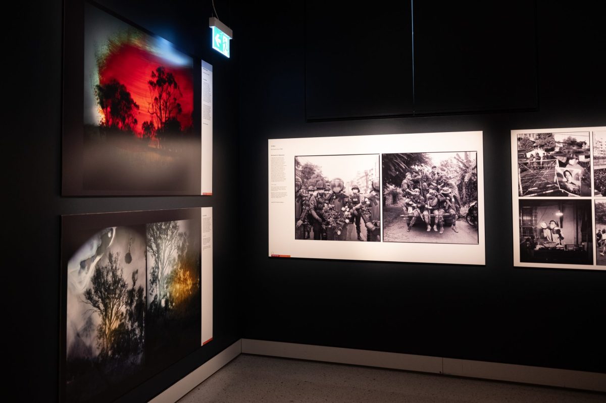 A exhibition display showing landscape photos an an angle on the left hand side and black photos of an army of soldiers on the back of the truck in the centre frame.