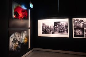 A exhibition display showing landscape photos an an angle on the left hand side and black photos of an army of soldiers on the back of the truck in the centre frame.