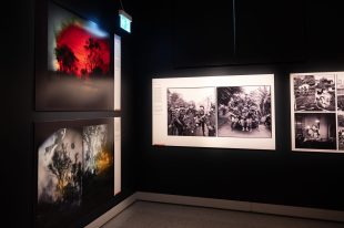 A exhibition display showing landscape photos an an angle on the left hand side and black photos of an army of soldiers on the back of the truck in the centre frame.