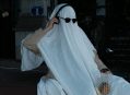 A person in a ghost costume with sunglasses and headphones is on the phone.