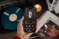 A photo of someone holding a phone that is playing a Taylor Swift album. In the background is a Taylor Swift viynl record.