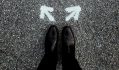 two black shoe clad feet with arrows facing in opposing directions on the ground. visual arts public sector