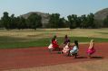 seven dark-skinned girls wearing brightly coloured dresses run on a racing track, with grass, trees and a bare hill rising towards a blue sky visible benhind them. The photo illustrates ArtsHub's On the move column, a weekly round-up of arts sector appointments across Australia.