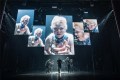 An image from the Broadway production of The Picture of Dorian Gray, with Tony-Award winning actor Sarah Snook peering into a camera and being broadcast across multiple screens.