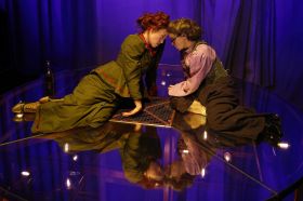 Two women crouched down, wearing period costume. Their heads are touching.