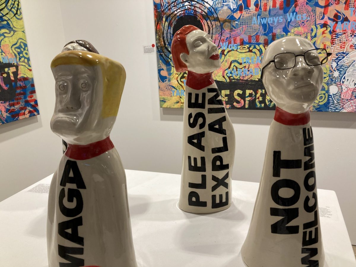 Ceramic figures with arm and legless bodies and heads identifiable as Pauline Hanson and Donald Trump and another bespectacled bald figure. The words 'PLEASE EXPLAIN' and 'MAGA' are painted down the bodies. 'Talking Heads' by Simone Arnol and Philomena Yeatman, , CIAF 2025 Art Fair Showcase, installation view. Photo: ArtsHub.