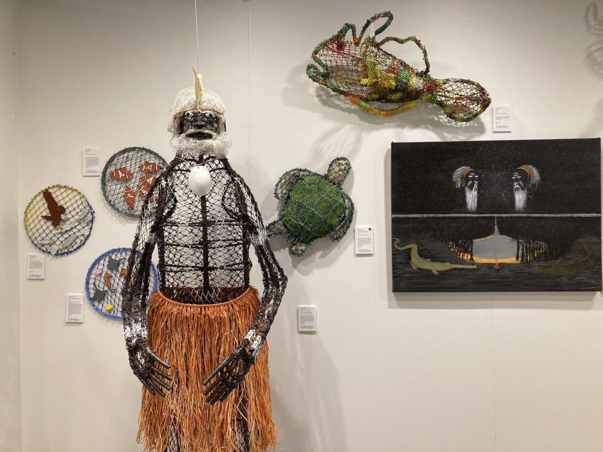 various soft sculptures made out of ghostnet and found objects, including wall hanging, a painting and a male figure. L-R: 'Sea Eagle' (2025) by Marlene Norman, ghostnet, wire and found objects; 'Manta Ray and Seahorses' (2025) by Thelma Norman, ghostnet, wire and found objects; 'Clown Fish (2025) by Mavis Benjamin, ghostnet, wire and found objects; 'Spirit Man' (2025) by Kim Norman, ghostnet, wire and found objects; 'Sea Turtle' (2025) by Alma Norman and Minh Permin, ghostnet, wire and found objects; 'Toad Fish'(2024), ghostnet, wire and found objects; 'Freshwater and Saltwater Crocodile Story' (2025) by Maurice Charlie, acrylic on Belgian linen; installation view. CIAF 2025 Art Fair Showcase.