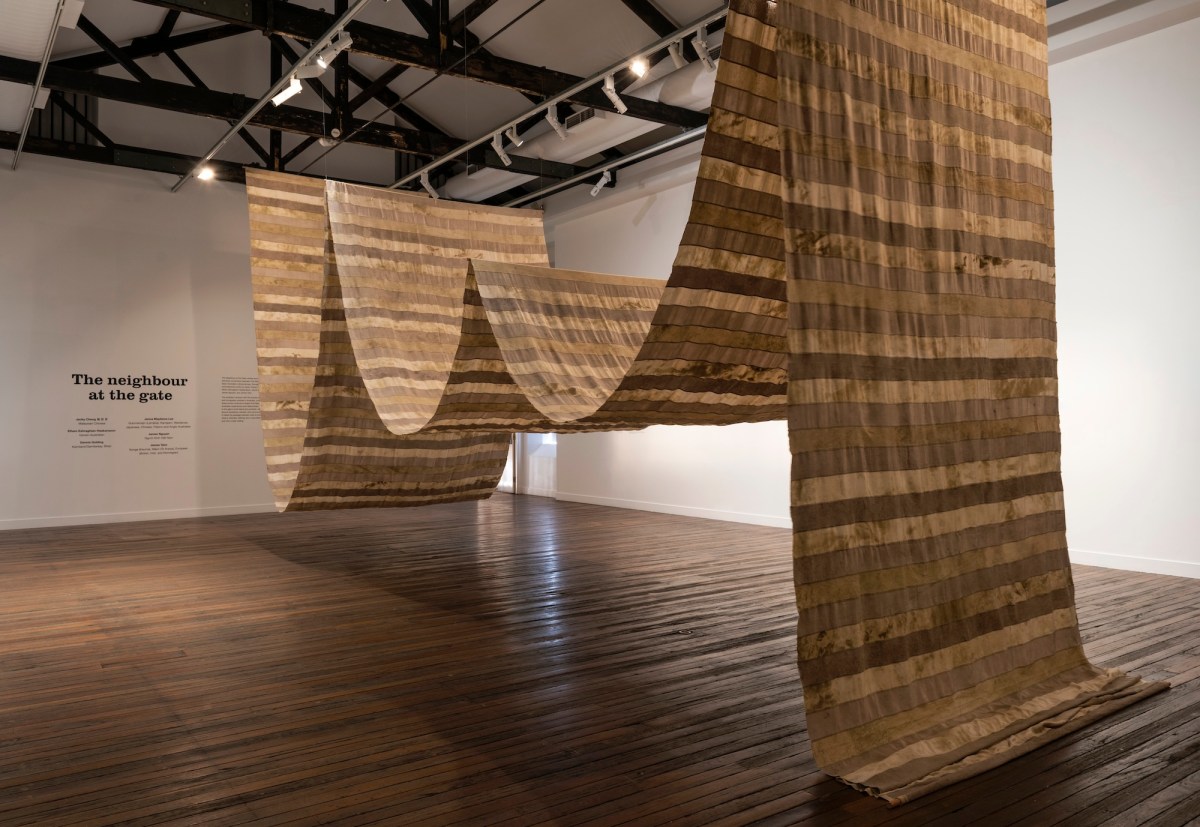 Installation view in gallery of a long textile artwork suspended from ceiling James Nguyen.