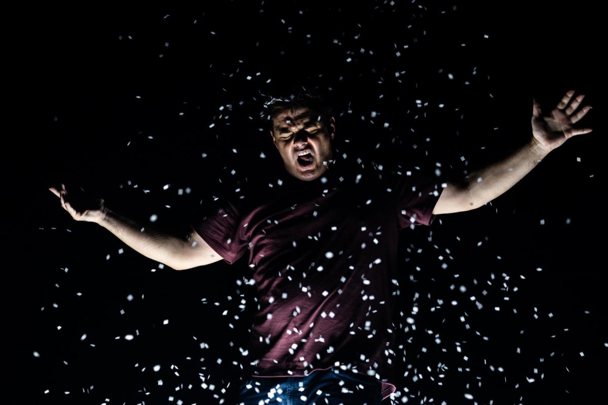 A man with his arms outstretched with white confetti falling over him.