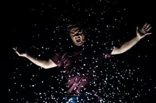 A man with his arms outstretched with white confetti falling over him.