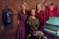 Three mature, fair-skinned female philanthropists pose together with objects recently acquired for the Australian Performing Arts Collection: a black leather jacket bedazzled with sequins, some of which spell out the word 'Olivia'; a glittering red gown, and a blue piano.