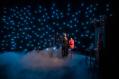 A woman in black is standing in mist. Around her a small lights that look like stars in the production of The Audition.