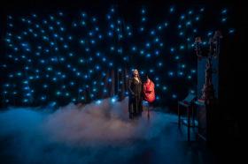 A woman in black is standing in mist. Around her a small lights that look like stars in the production of The Audition.