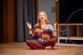 A middle aged, fair skinned women sits with legs crossed and hands raised in a rehearsal room. This is actor Rebecca Gibney in a scene from Sydney Theatre Company’s 'Circle Mirror Transformation', 2025.