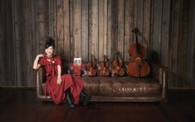 Photo of Hiromi wearing a red dress sitting on a leather couch alongside four string quartets.