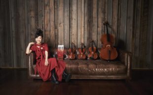 Photo of Hiromi wearing a red dress sitting on a leather couch alongside four string quartets.