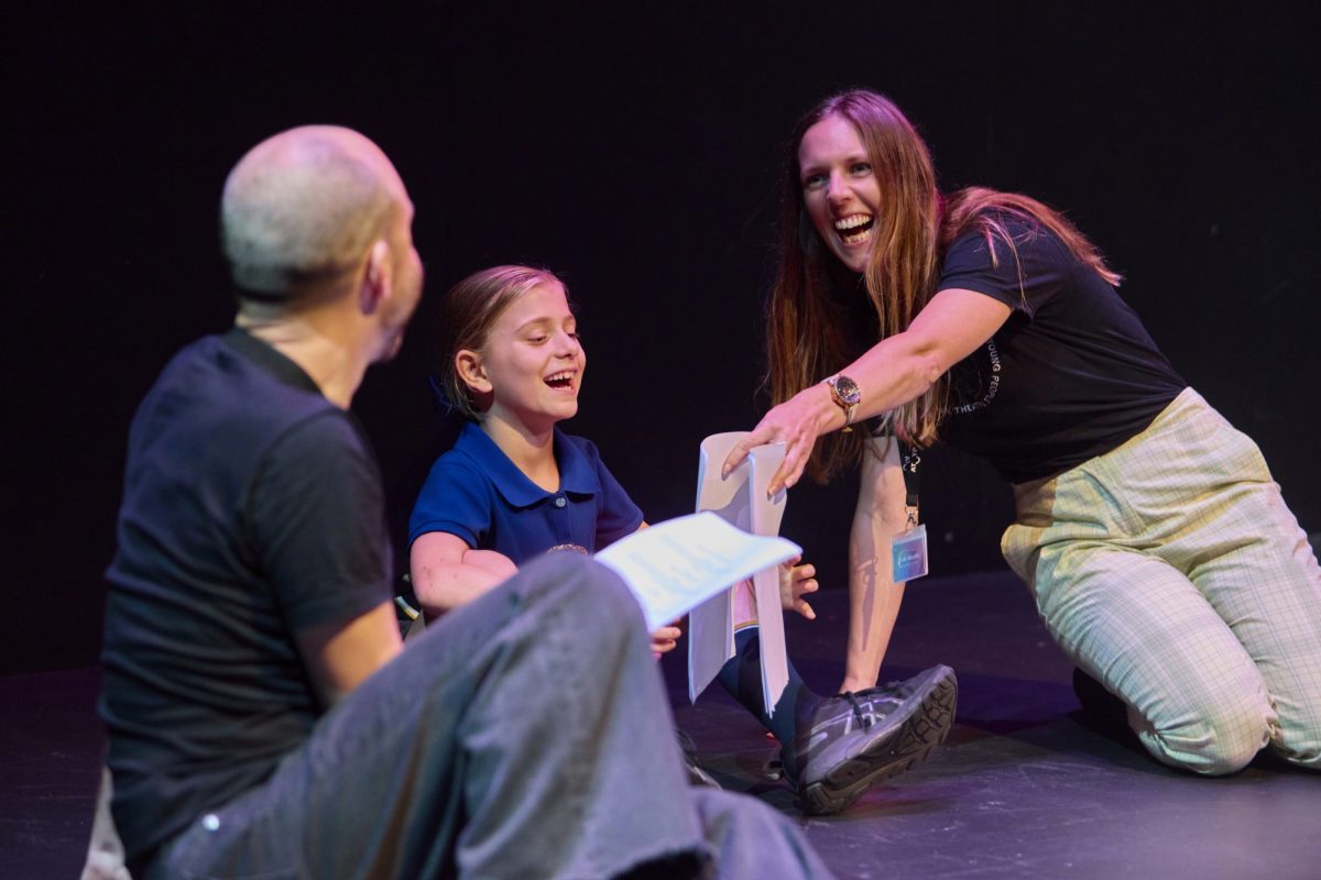 A young girl, man and woman sit on a stage with a script rehearsing. Audrey. Make-A-Wish. AYPT.