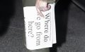 A pale hand holding a folded newspaper held vertically with the text ‘Where do we go from here?’