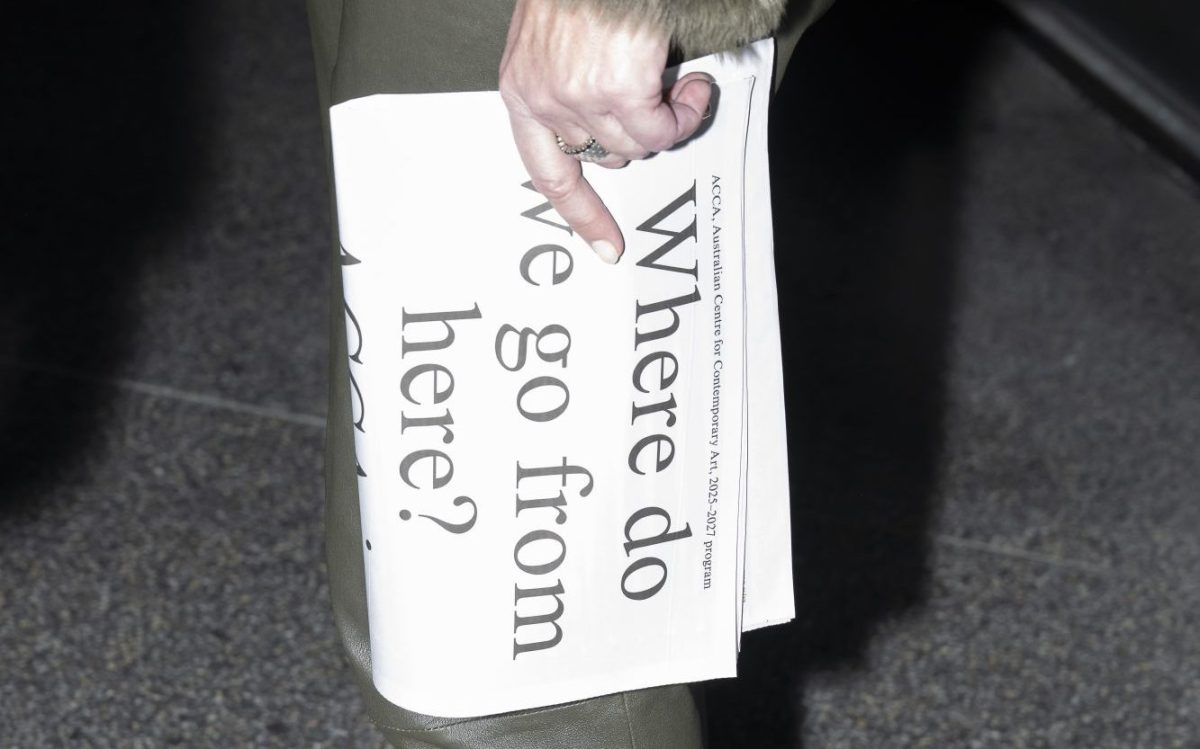 A pale hand holding a folded newspaper held vertically with the text ‘Where do we go from here?’