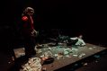 A woman in a red top i staring down at a man who is on the ground surrounded by debris.