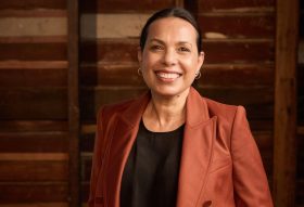 A smiling First Nations woman with a black top and russet jacket, her hair is parted and slicked back. Frances Rings - what I've learned