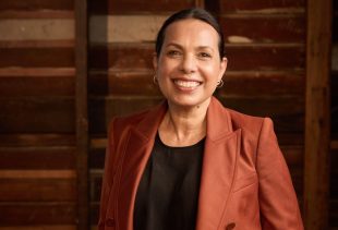 A smiling First Nations woman with a black top and russet jacket, her hair is parted and slicked back. Frances Rings - what I've learned