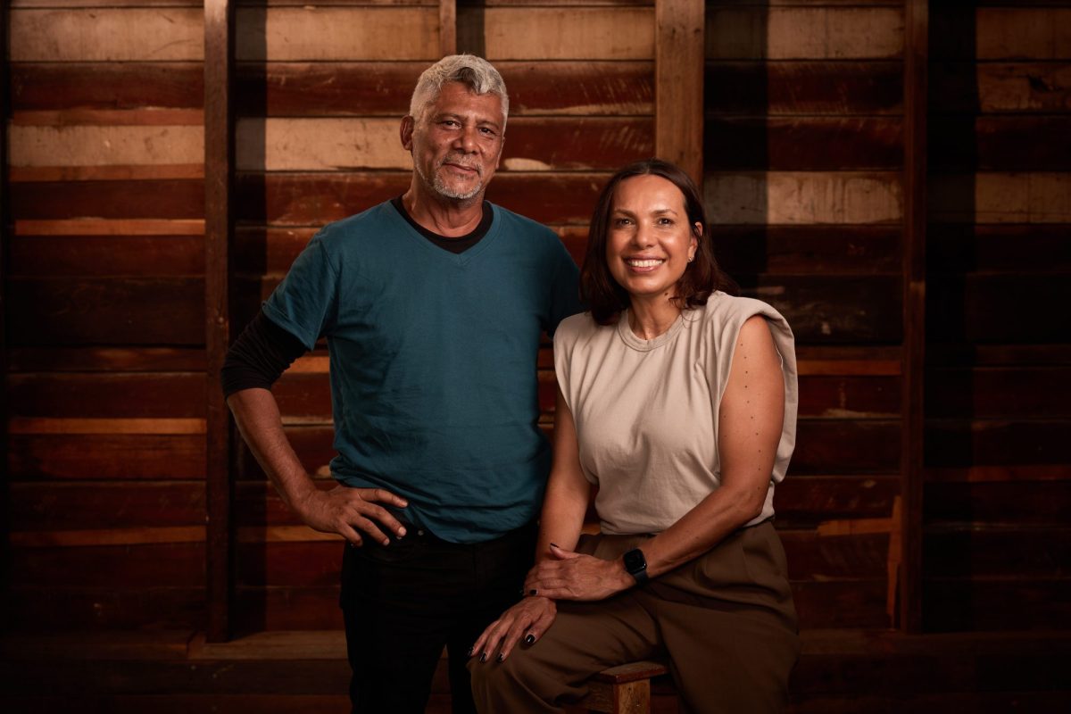 A First Nations man with white hair and blue/green T shirt stands next to a seated First Nations woman in a sleeveless cream T shirt and brown trousers. Frances Rings - what I've learned