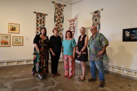 Five middle-aged Caucasian artists standing in a gallery with beige walls and artworks, including four long hanging tapestry or textile pieces. 2025 Miles Franklin Award, Siang Lu. Arts prize winners, recipients, shortlists.