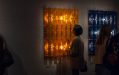 Two large illuminated relief works, one orange and one dark blue, displayed on a wall. A figure is observing the orange work. free exhibitions.