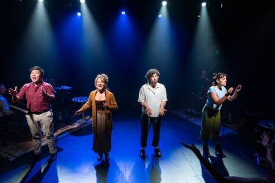 Two men and two women in casual clothes on stage, singing.