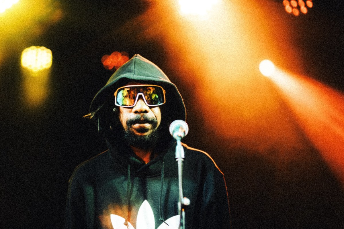 Indigenous man wearing hoodie and glasses on stage with orange lights. NAIDOC