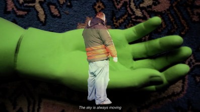 A man standing in front of a giant green hand. Desire Is a Machine.