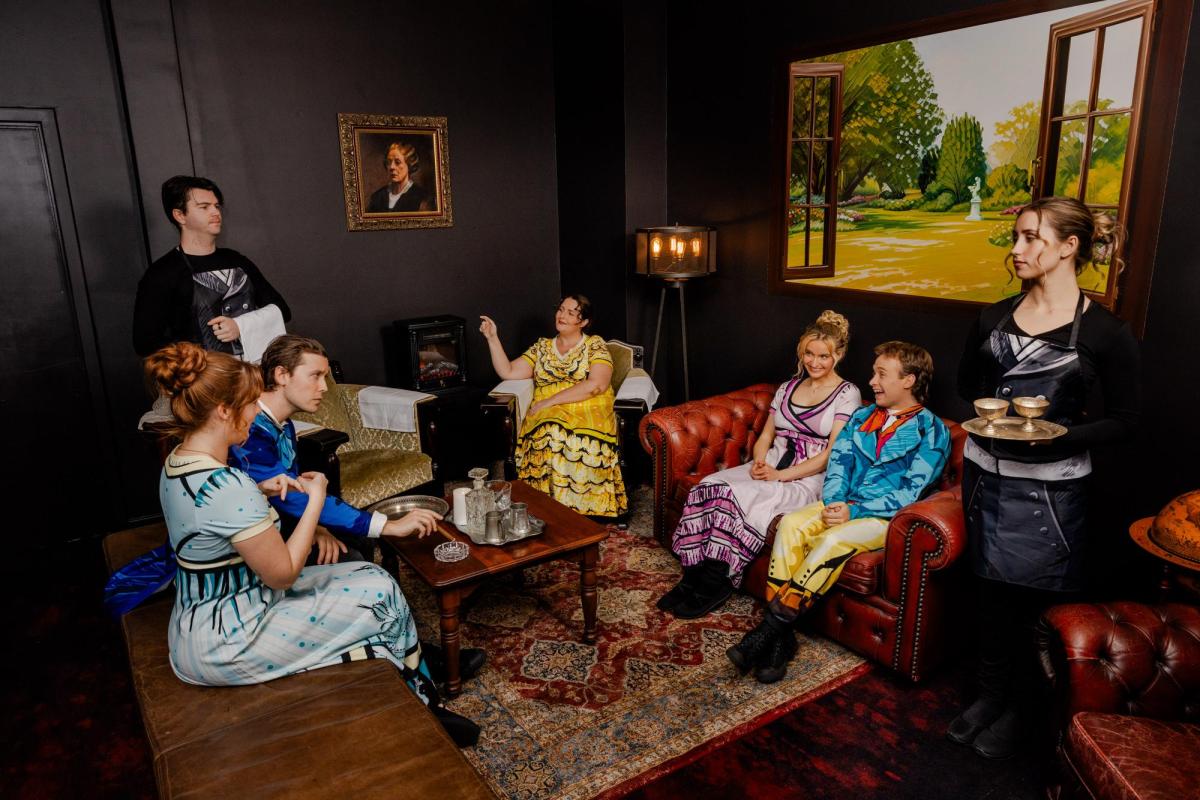 A group of people in Regency period costume in a parlour room. Plied and and Prejudice.