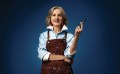 Image of woman wearing an apron and holding a paintbrush against blue background. Art prize