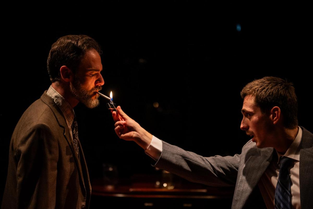 Two men in suits, one lighting a cigarette for the other. Smokescreen