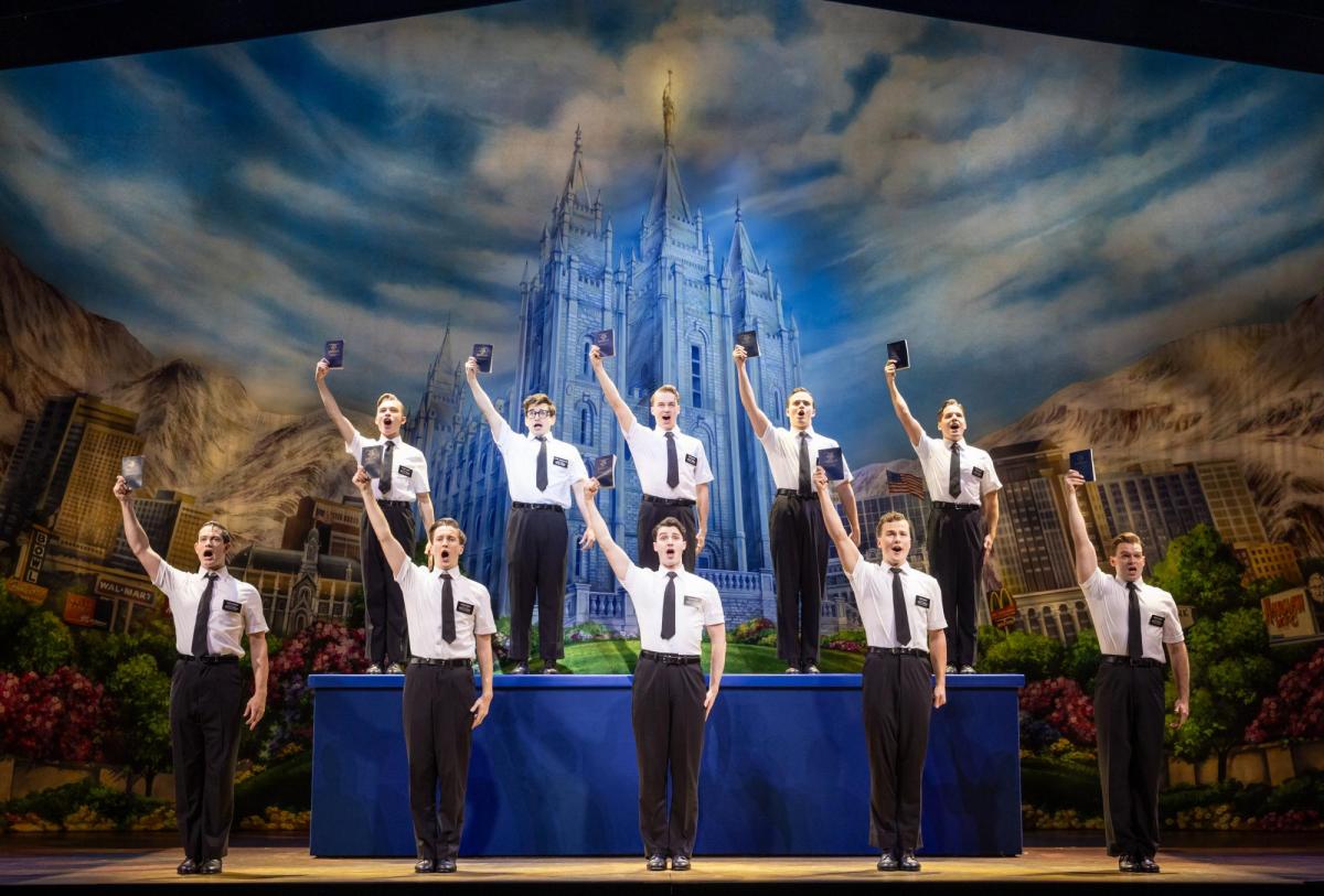 A group of men in white shirts and black ties stand in formation. The right arms are raised with a bible.