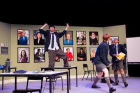 A classroom scene in Trophy Boys, with three students. One is standing on a table.