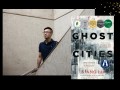 Two panels. The wider one has an Asian man in a black top half hidden by a diagonal stairwell. The small panel features a book cover' Ghost Cities.'