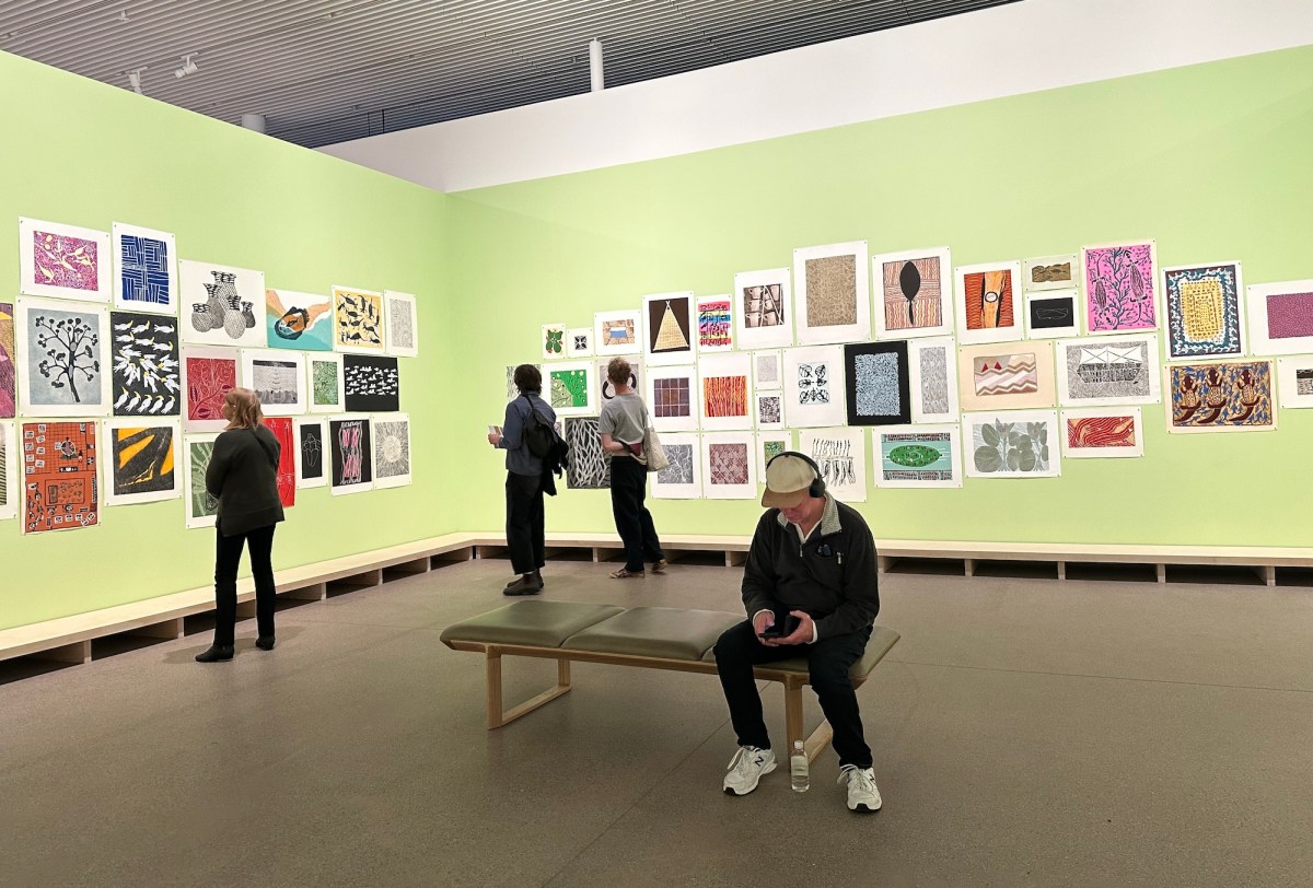 people in gallery with light green walls, displaying prints on paper. Yirrkala