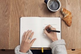 A view from above as someone handwrites into a notebook, thereby avoiding any issues of AI copyright.