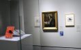 A painting of a man in profile. There is an orange book, 'Just So Stories' in a glass case and some other documents next to the painting.