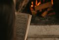 art books, a woman reads a book in front of an open fire.