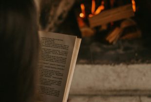 art books, a woman reads a book in front of an open fire.