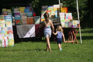 A young girl is holding the hand of a toddler girl. They are walking towards some picture books.