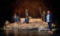 The cast of The Visitors - Seven people in suits either sitting or standing on a rock-like formation.