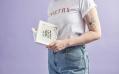 A person with the word poetry on a white t-shirt. They are wearing jeans and holding a book. Poetry Month. Red Room Poetry.